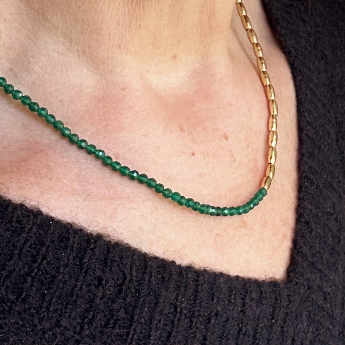 a close up image of mdels neck wearing a gold and green faceted gemstone necklace