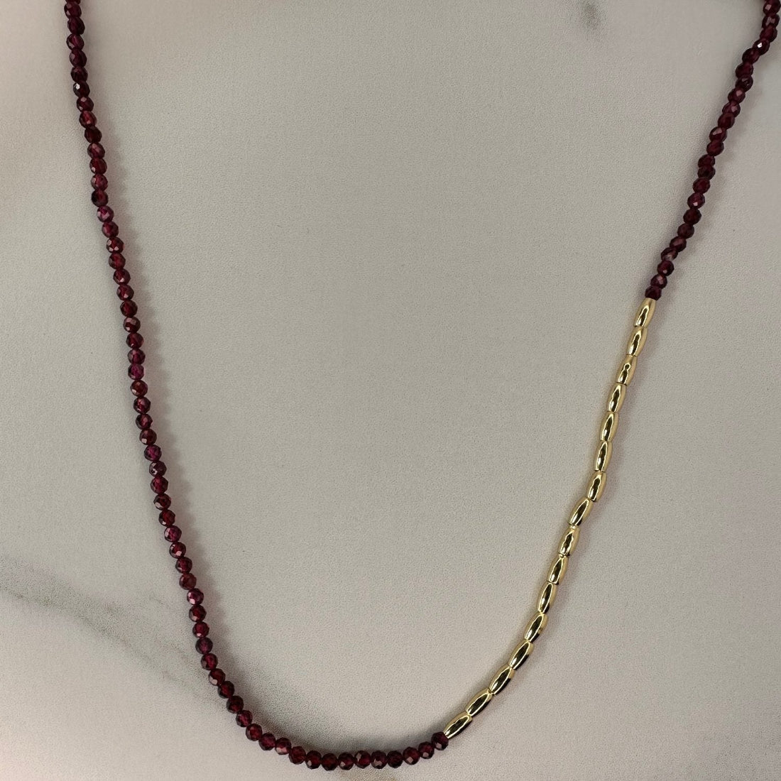 a gold nugget necklace with red sparkling cubic zirconia beads ideal for layering displayed on a white ground