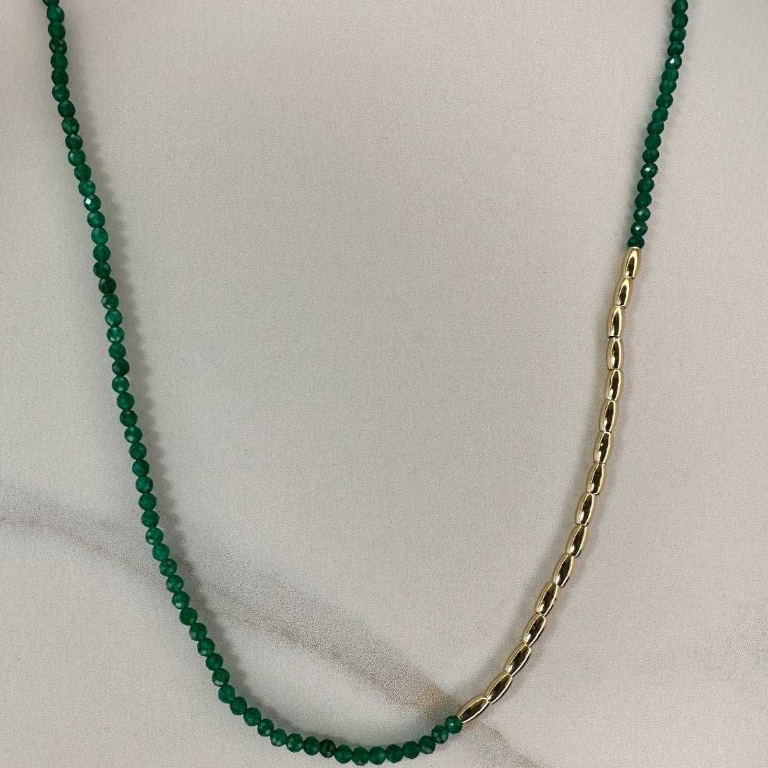 a gold nugget necklace with green  sparkling cubic zirconia beads ideal for layering displayed on a white ground