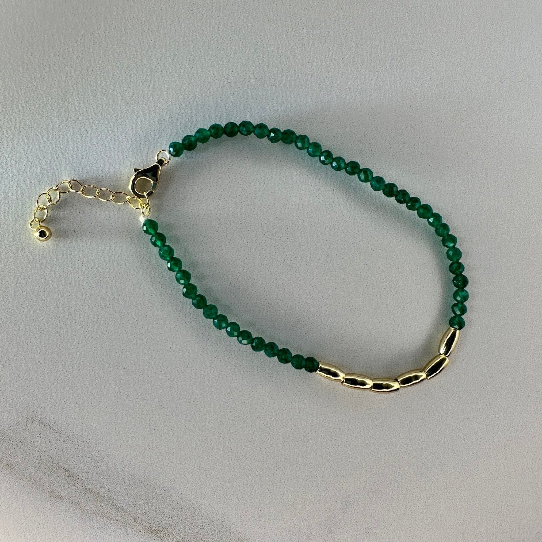 a gold nugget bracelet with green  sparkling cubic zirconia beads ideal for layering displayed on a white ground