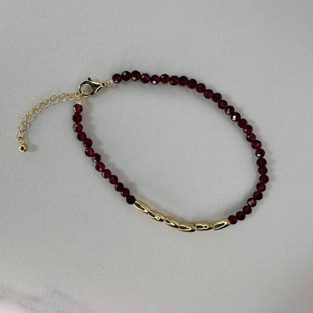 a gold nugget bracelet with red sparkling cubic zirconia beads ideal for layering displayed on a white ground