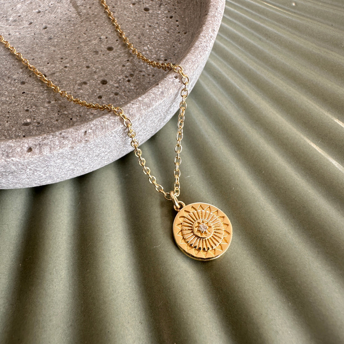 Talisman sunburst modern gold necklace with a circular pendant on a textured surface