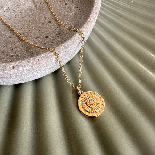 Talisman sunburst modern gold necklace with a circular pendant on a textured surface