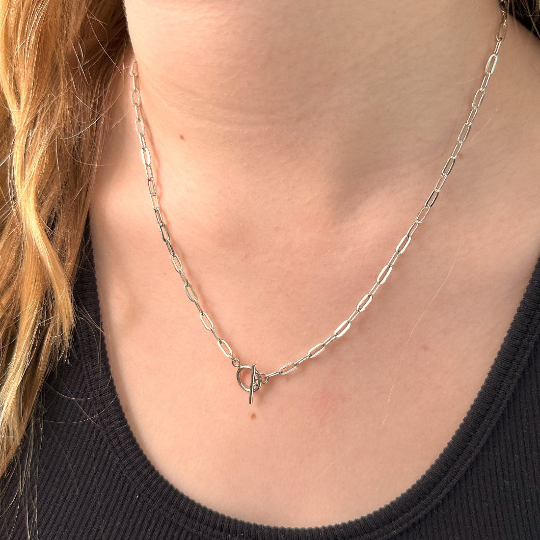 A person wearing a silver T-bar toggle paperclip chain necklace with a sleek, modern design.