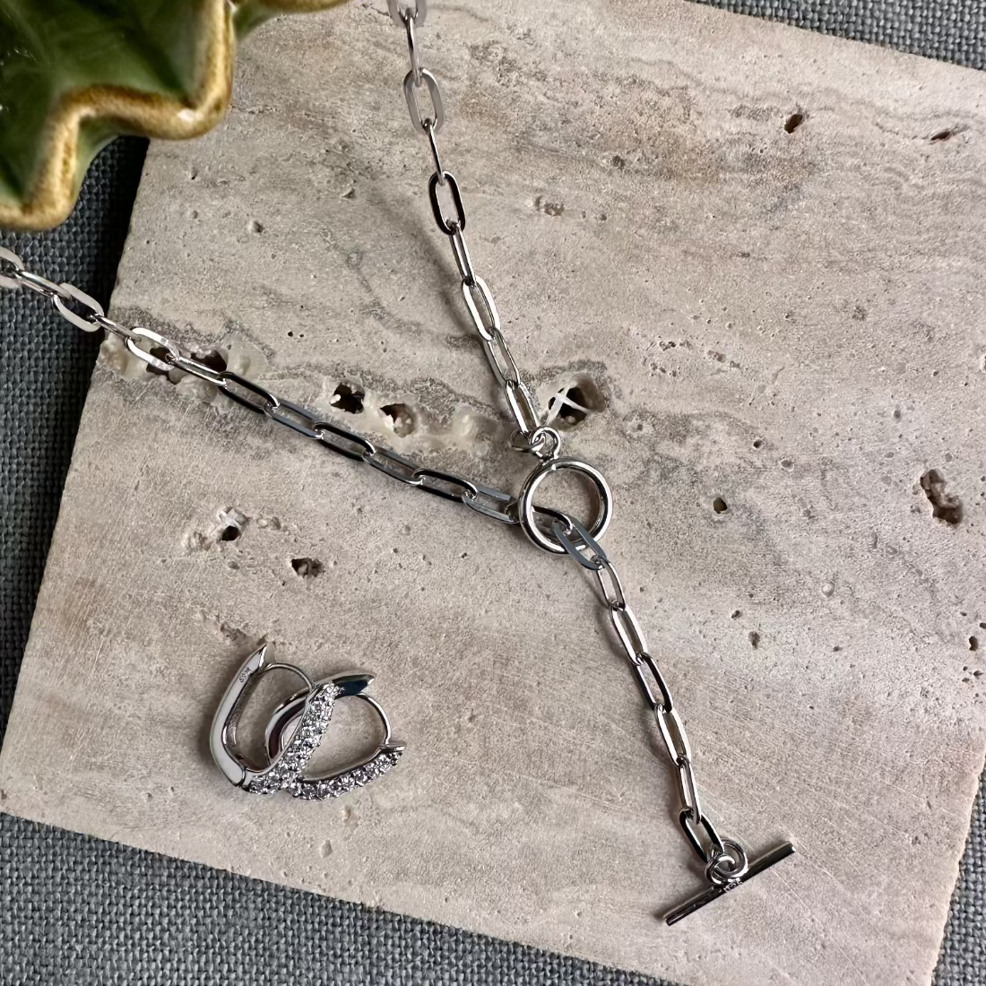 a silver T-bar toggle paperclip chain necklace with a sleek, modern design along with gemstone silver earrings laid on tile ground