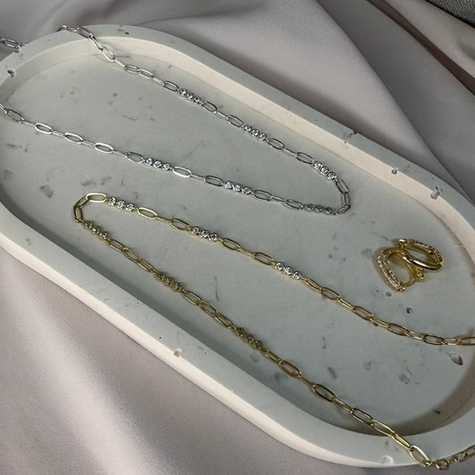 delicate papreclip chain neckalce and bracelet with triple cluster of white gemstones sparkling laid on cream ground