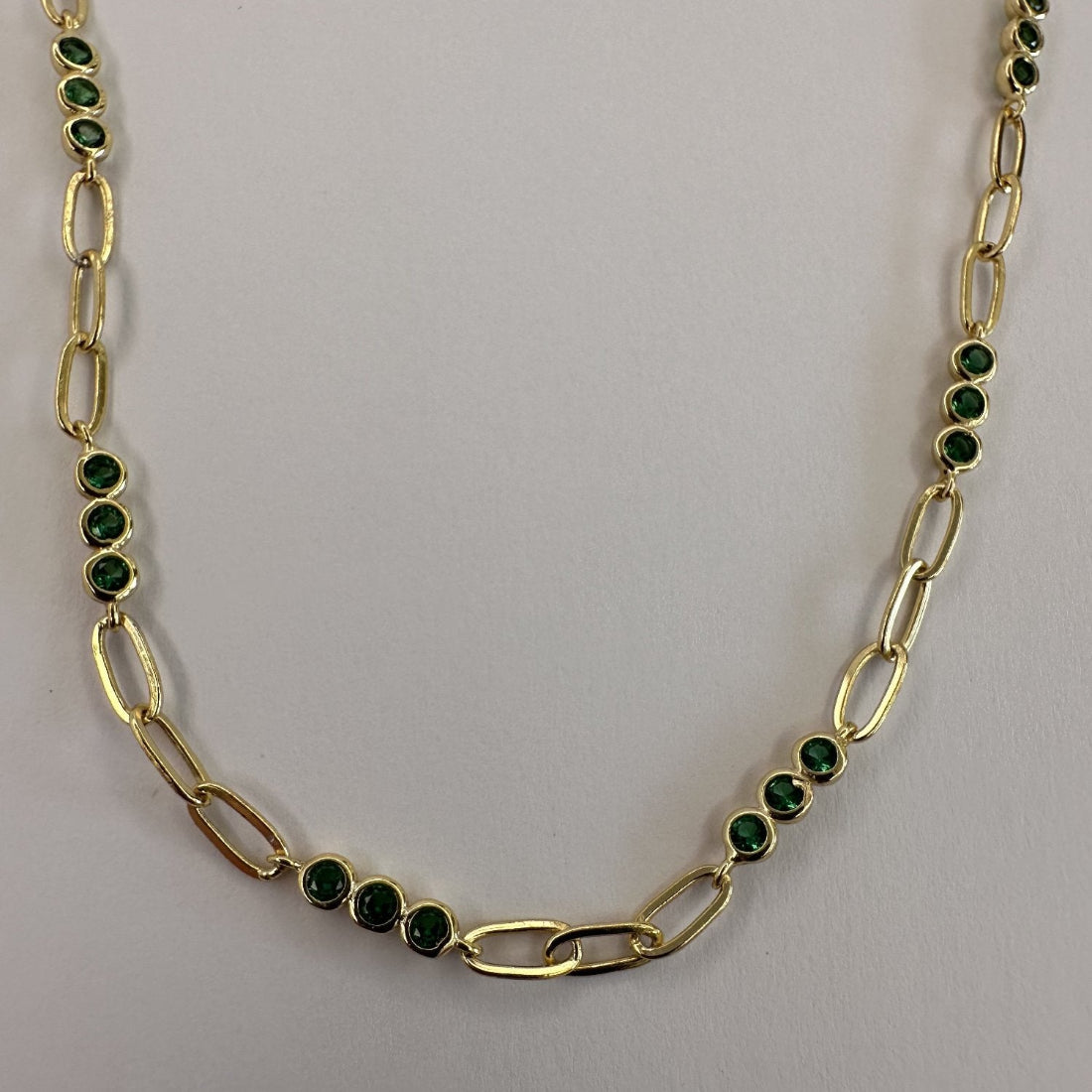 a close up image of a paperclip modern chain link necklace with triples of gemstones, laid on a white ground