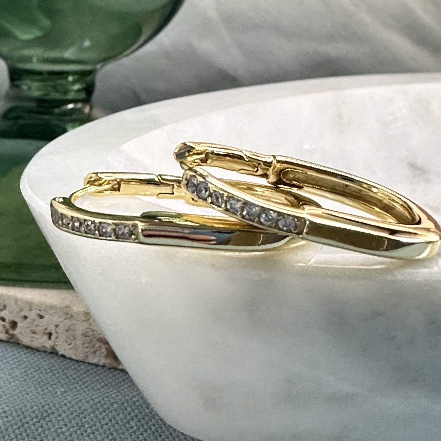 gold oval hoop earrings with gemstones on a marble dish surface.